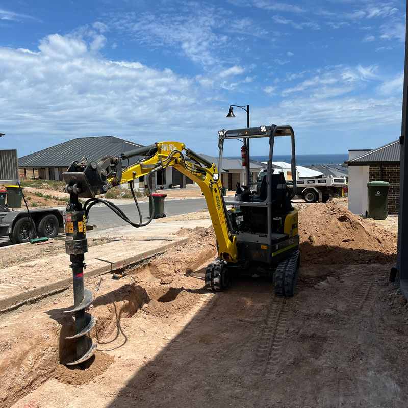 Mini excavator with an auger attachment on a cleared block in a new housing estate