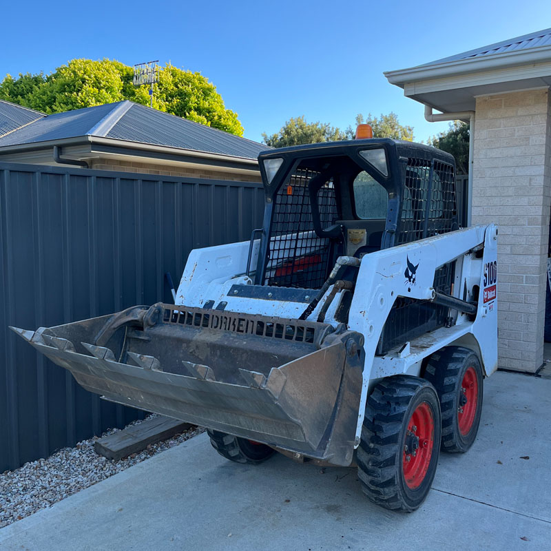 Skid steer loader with its bucket down on a concrete driveway beside a house