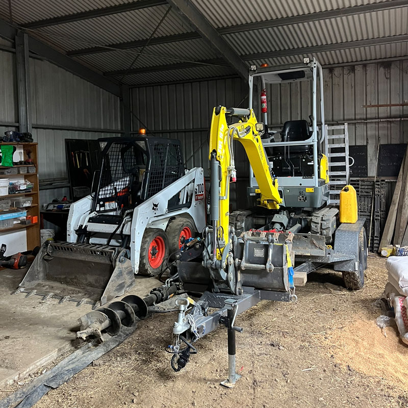 Mini excavator on a trailer and a skid steer loader parked in a shed