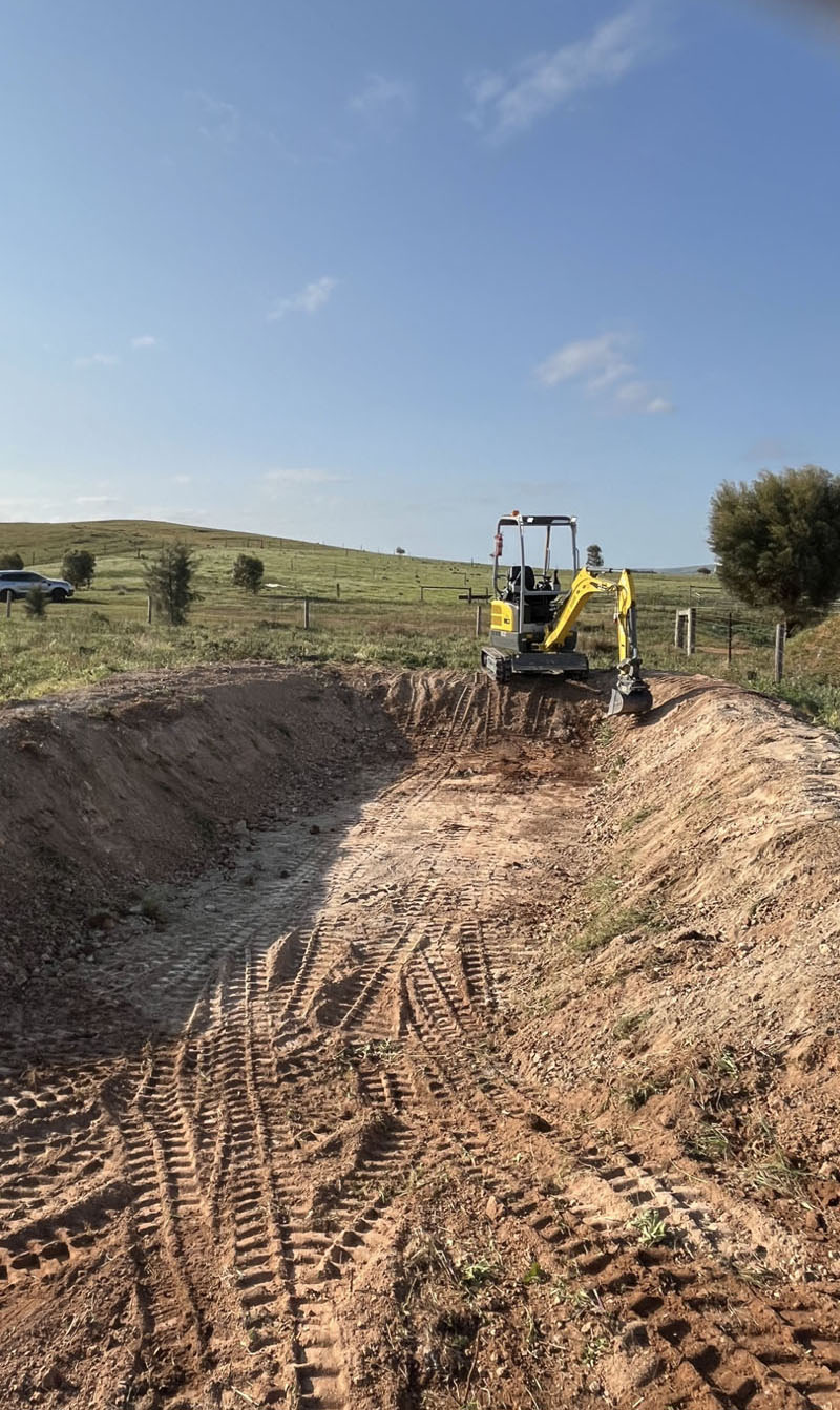 Long excavated cut in a sloping paddock with a mini excavator at the far end