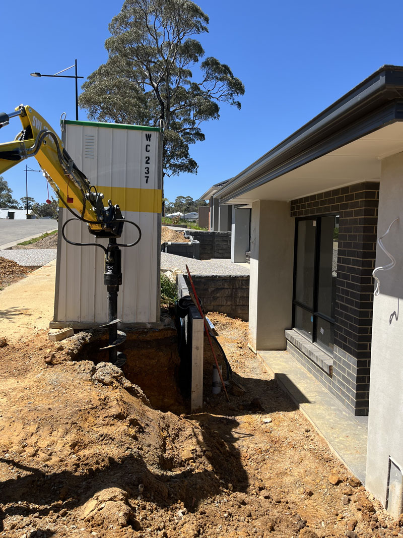 Mini excavator auger working in an excavation beside a new brick house