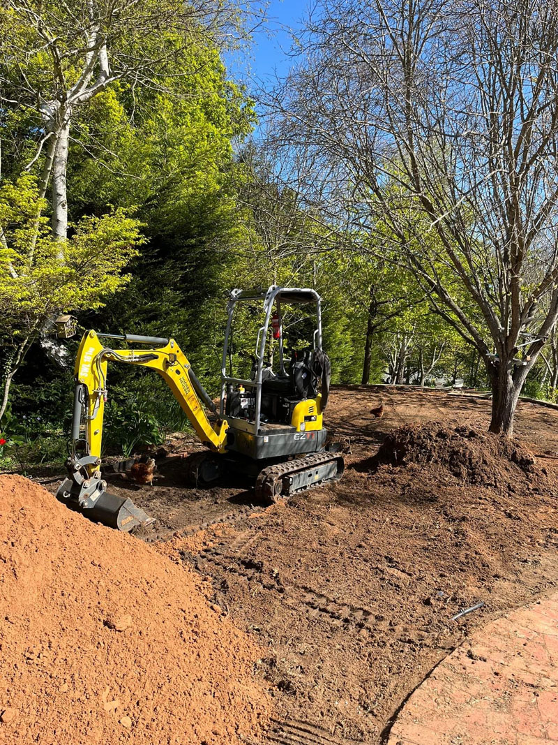 Closer view of a mini excavator digging beside a mound of red soil in a garden
