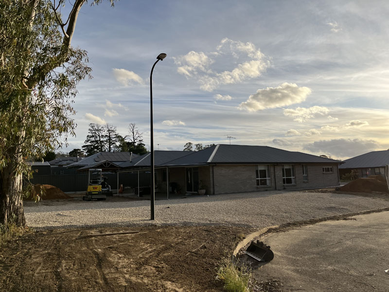 Levelled soil around a new house on a corner block at sunset, mini excavator behind
