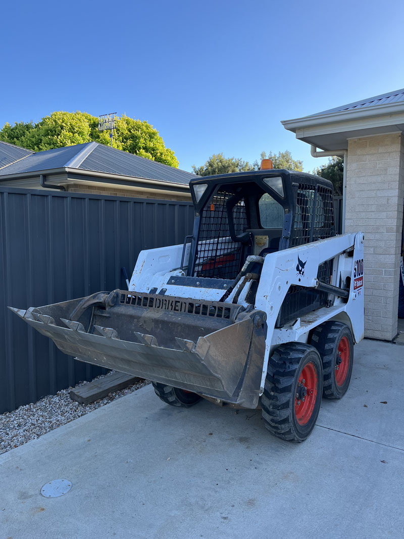 Skid steer loader with its bucket down on a concrete driveway beside a house