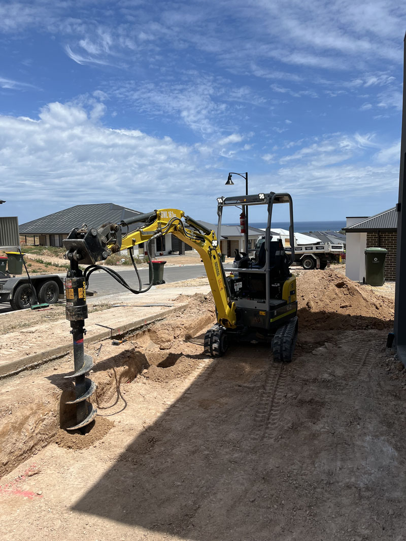 Mini excavator with an auger attachment on a cleared block in a new housing estate