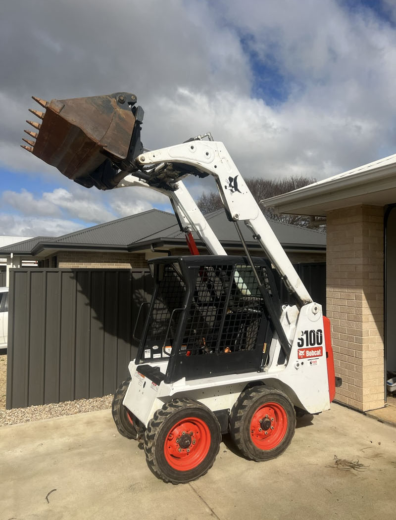 Skid steer loader with its bucket raised high on a concrete driveway