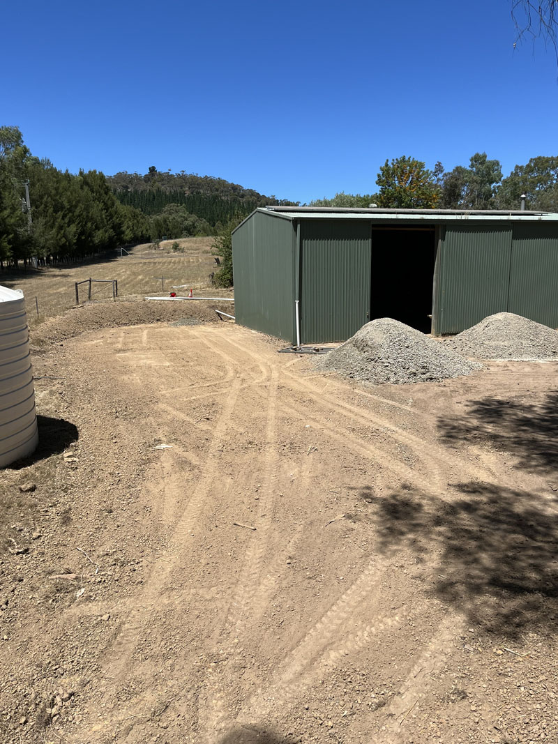 Levelled dirt pad leading to a green shed, with piles of gravel