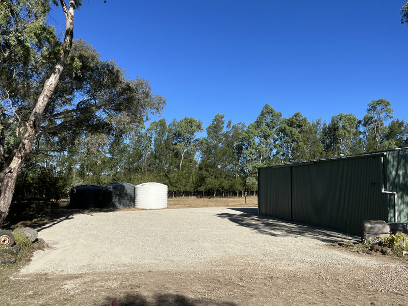 Gravel hardstand in front of a large green shed and water tanks