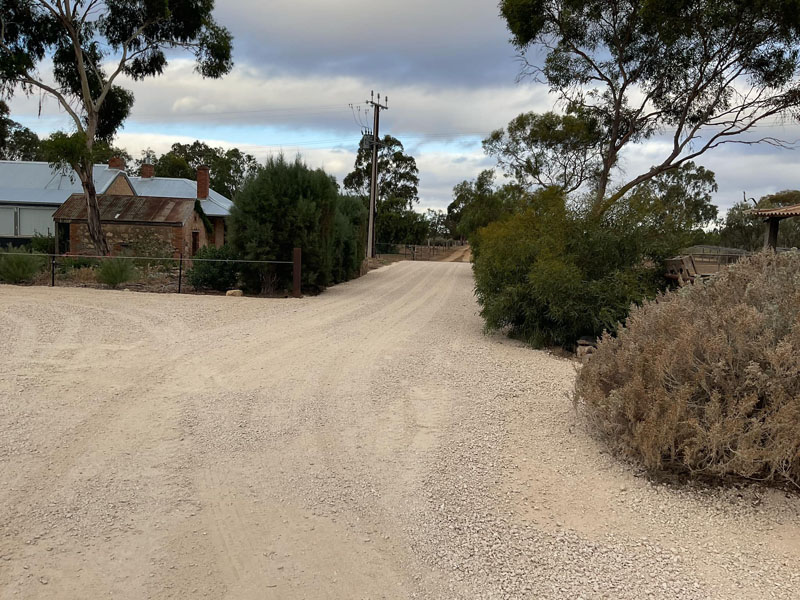 Wide gravel road past trees and old stone buildings