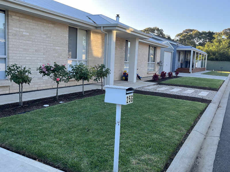 New lawn and garden beds in front of a new brick house with a letterbox