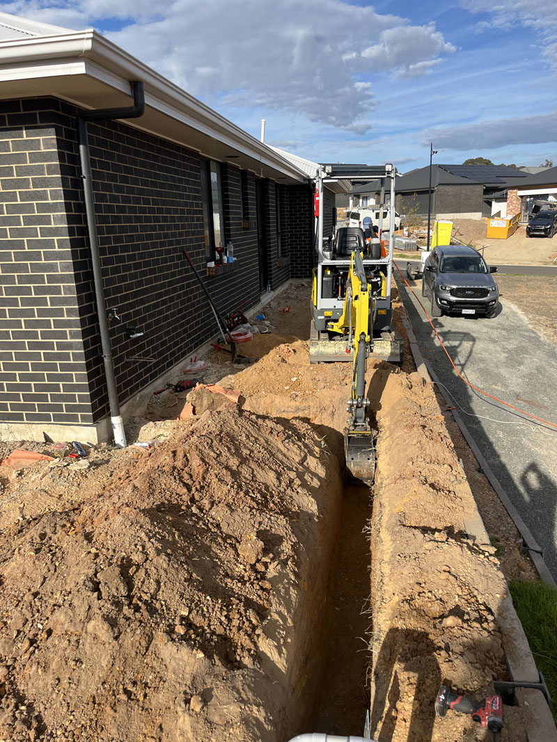 Mini excavator digging a long trench beside a new brick house