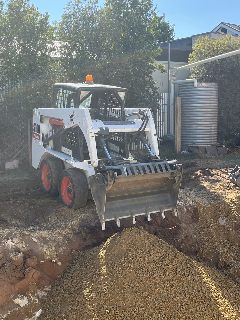 Skid steer loader moving a pile of sandy fill in an excavated yard