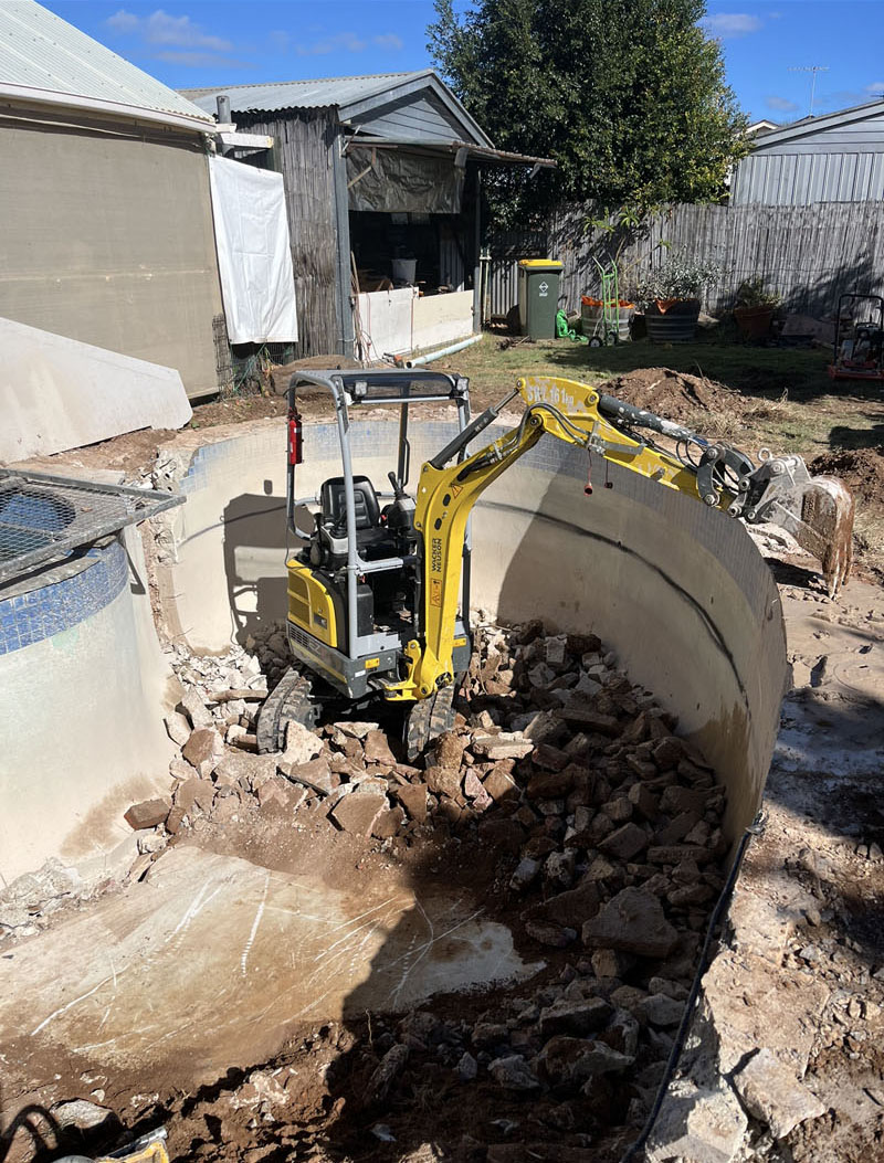 Mini excavator filling an old in-ground pool with broken concrete