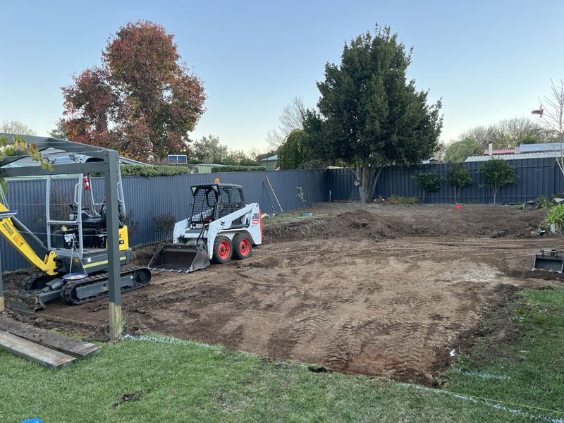 Mini excavator and skid steer loader levelling a fenced backyard