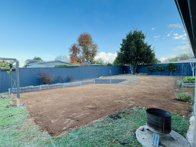 Levelled bare soil across a backyard, with a fire pit on the lawn