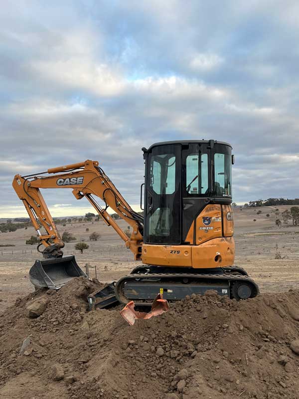 Orange Case excavator on a mound of dirt in an open paddock