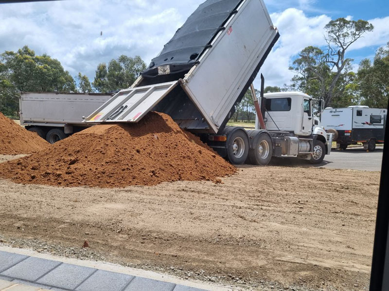 Tipper truck unloading a load of red soil onto a levelled site